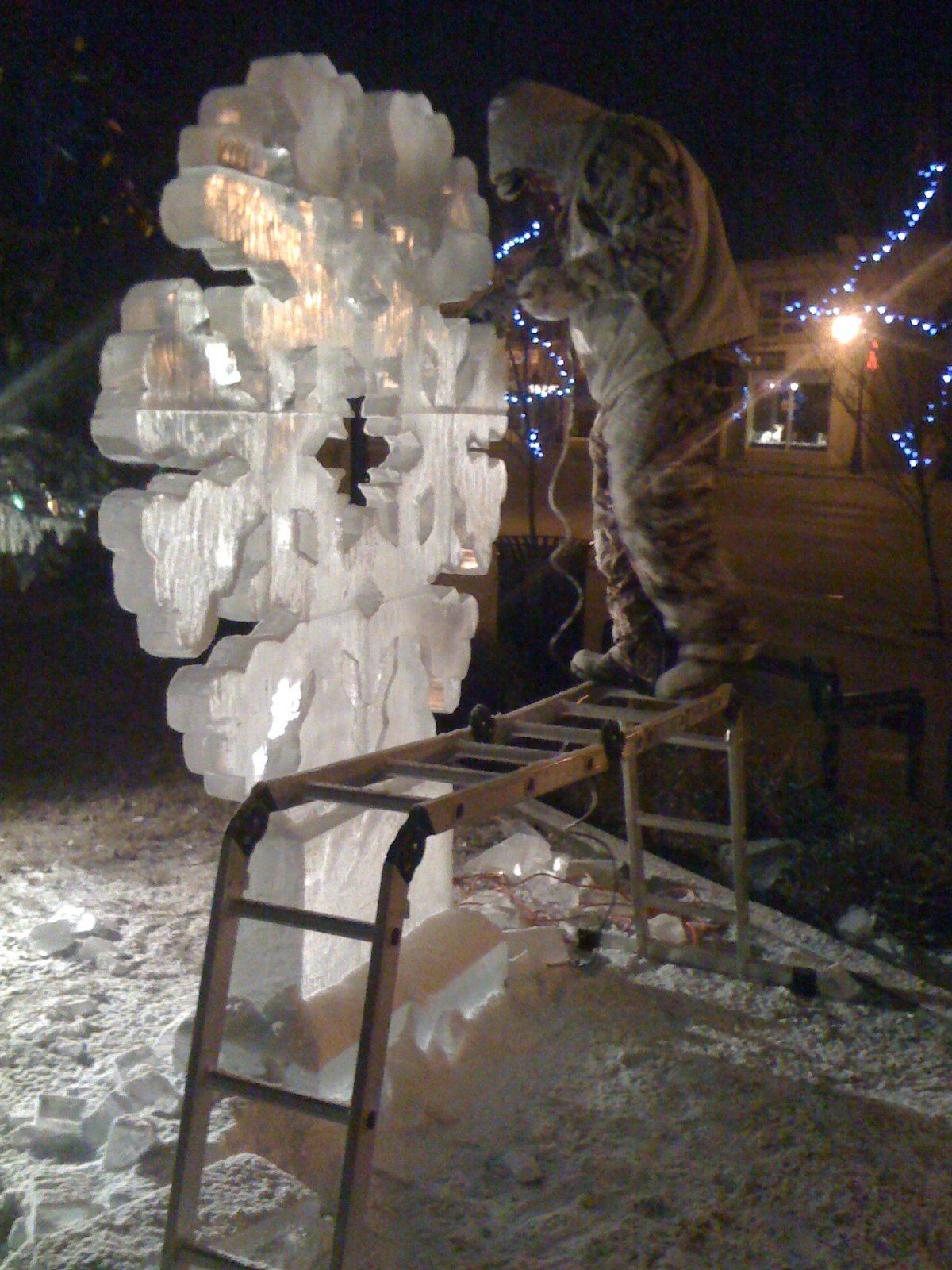 Sculptor on ladder with snowflake ice sculpture at night